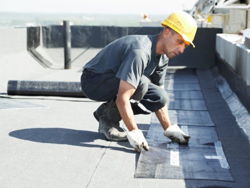 Roofer preparing part of bitumen roofing felt roll for melting by gas heater torch flame